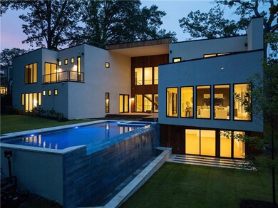 Back of property at dusk featuring a balcony, a yard, stucco siding, and a pool with connected hot tub