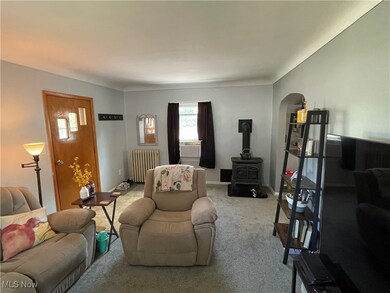 Living room featuring radiator heating unit, carpet floors, arched walkways, and a wood stove