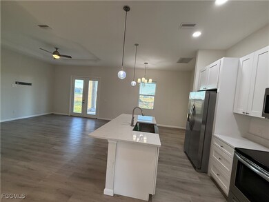 Kitchen with appliances with stainless steel finishes, ceiling fan, hanging light fixtures, white cabinetry, and open floor plan