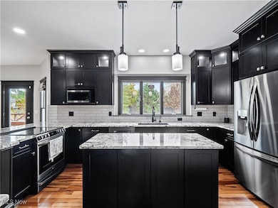 Kitchen featuring dark cabinetry, appliances with stainless steel finishes, light stone countertops, a kitchen island, and recessed lighting