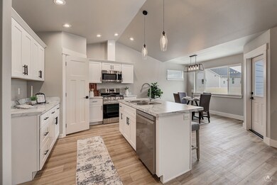 Kitchen with stainless steel appliances, light countertops, vaulted ceiling, decorative light fixtures, and white cabinetry