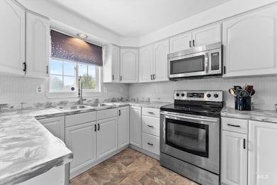 Kitchen featuring appliances with stainless steel finishes, white cabinets, stone finish floors, and backsplash