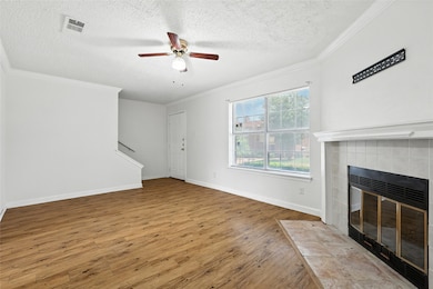 Unfurnished living room with a ceiling fan, a textured ceiling, wood finished floors, ornamental molding, and a tiled fireplace
