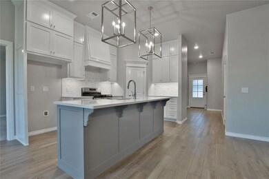Kitchen with an island with sink, decorative light fixtures, stainless steel range with gas cooktop, premium range hood, and white cabinetry