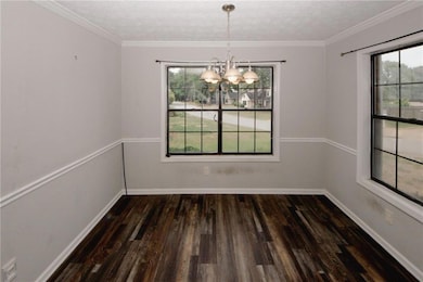 Unfurnished dining area with a chandelier, healthy amount of natural light, wood finished floors, baseboards, and a textured ceiling