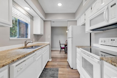 Kitchen featuring sink, white cabinets, light stone counters, light hardwood / wood-style floors, and white appliances