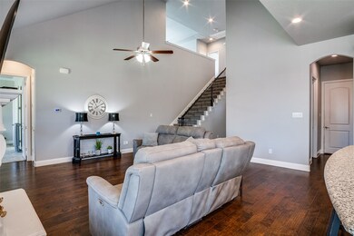 Living room featuring arched walkways, high vaulted ceiling, dark wood-style flooring, stairs, and ceiling fan