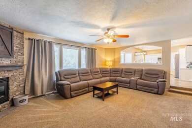 Living area with a textured ceiling, a ceiling fan, a stone fireplace, and light carpet