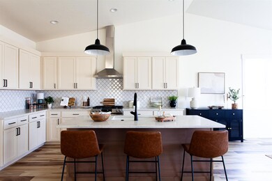 Kitchen with wall chimney range hood, vaulted ceiling, a breakfast bar area, backsplash, and light wood-style flooring