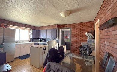 Kitchen featuring brick wall, freestanding refrigerator, light countertops, stainless steel microwave, and light floors