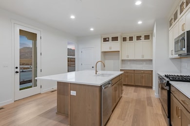 Kitchen with brown cabinets, glass insert cabinets, tasteful backsplash, appliances with stainless steel finishes, and a center island with sink