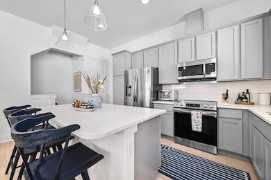 Kitchen featuring gray cabinetry, stainless steel appliances, hanging light fixtures, decorative backsplash, and recessed lighting