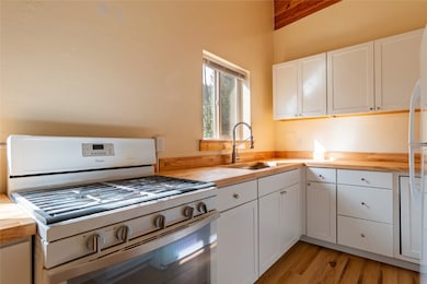 Kitchen with butcher block counters, white appliances, white cabinetry, and light wood-type flooring