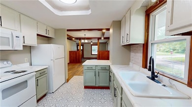 Kitchen with white appliances, backsplash, green cabinets, a peninsula, and light counters