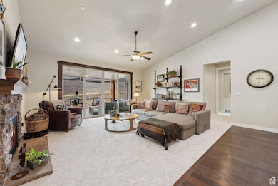 Living area with a ceiling fan, wood finished floors, a stone fireplace, baseboards, and recessed lighting