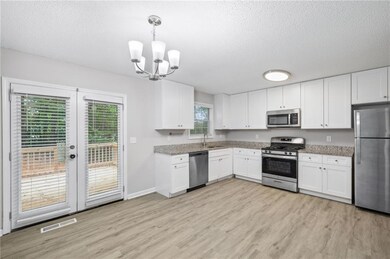 Kitchen with stainless steel appliances, light wood-style floors, white cabinetry, a chandelier, and a textured ceiling