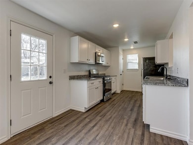Kitchen featuring appliances with stainless steel finishes, a sink, dark wood-style floors, baseboards, and white cabinetry
