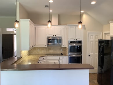 Kitchen featuring black appliances, decorative backsplash, hanging light fixtures, a peninsula, and dark countertops