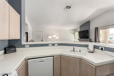 Kitchen with light brown cabinetry, tile countertops, dishwasher, a textured ceiling, and a peninsula