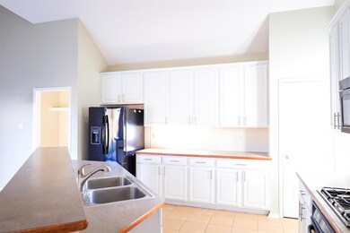 Kitchen with light tile flooring, sink, white cabinetry, and black fridge