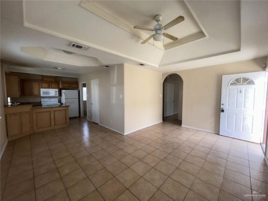 Unfurnished living room featuring a tray ceiling, a ceiling fan, tile patterned floors, and arched walkways