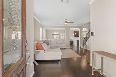 Living room featuring ornamental molding, dark wood-type flooring, stairs, arched walkways, and a ceiling fan