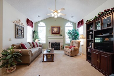 Living area featuring a ceiling fan, light carpet, a tile fireplace, healthy amount of natural light, and vaulted ceiling