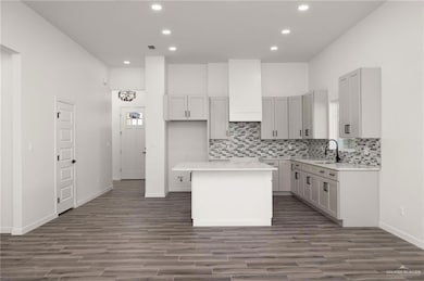 Kitchen with a center island, recessed lighting, tasteful backsplash, dark wood finished floors, and light stone counters