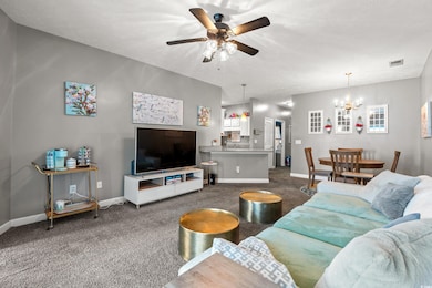 Living room with dark colored carpet, ceiling fan, and a chandelier