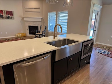Kitchen featuring light wood-type flooring, dark cabinets, appliances with stainless steel finishes, a fireplace, and light stone countertops