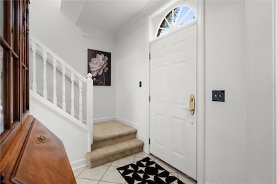 Foyer with crown molding, light tile patterned flooring, and stairs