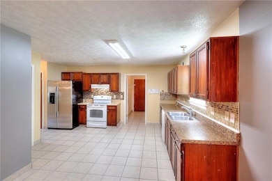 Kitchen with white electric range oven, stainless steel fridge with ice dispenser, backsplash, light tile patterned flooring, and a textured ceiling
