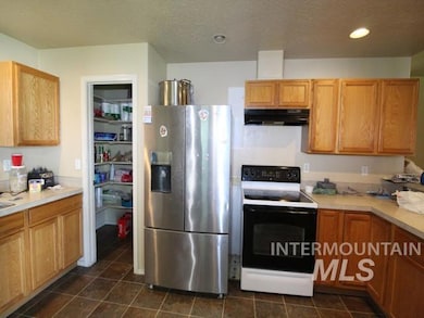Kitchen with electric range, stainless steel fridge with ice dispenser, under cabinet range hood, light countertops, and dark tile patterned flooring