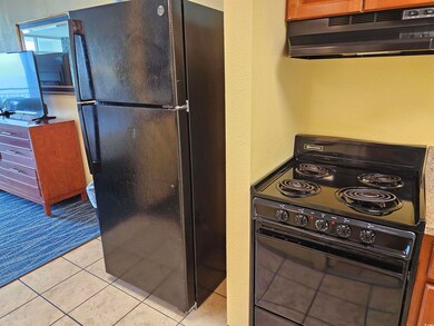 Kitchen with black appliances, under cabinet range hood, and light tile patterned floors