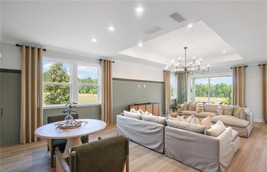 Living area with a chandelier, healthy amount of natural light, a tray ceiling, light wood-type flooring, and recessed lighting