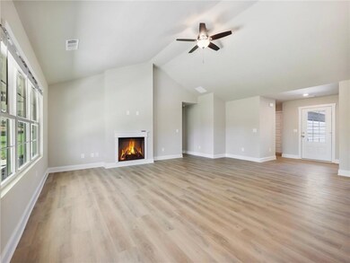 Unfurnished living room featuring a warm lit fireplace, light wood-type flooring, a ceiling fan, lofted ceiling, and baseboards