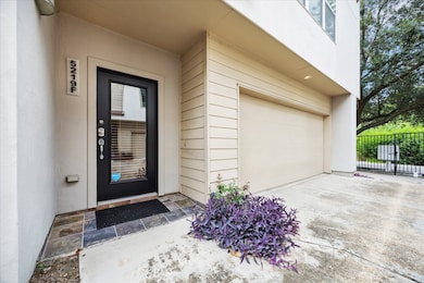This townhome entry offers a welcoming first impression with a sleek black front door, slate tile threshold, and a tidy planting bed for a pop of color. The attached two-car garage and gated driveway provide added convenience and security.