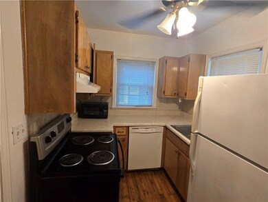 Kitchen with white appliances, under cabinet range hood, light countertops, and dark wood-type flooring