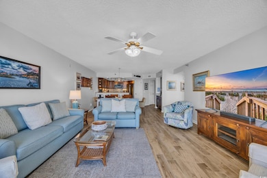 Living room with light wood-style flooring, a ceiling fan, baseboards, and a textured ceiling