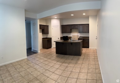 Kitchen featuring dark countertops, dark brown cabinets, recessed lighting, light tile patterned flooring, and a kitchen island with sink