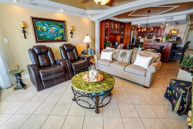 Living area featuring crown molding, a chandelier, decorative columns, a raised ceiling, and light tile patterned floors