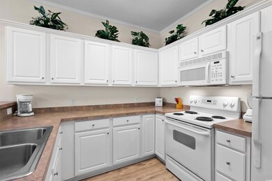 Kitchen with white appliances, white cabinetry, ornamental molding, a textured ceiling, and light wood-type flooring