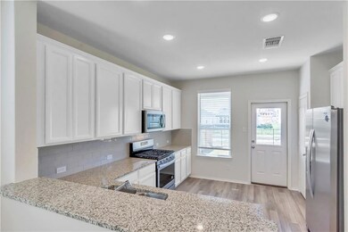 Kitchen with appliances with stainless steel finishes, white cabinetry, light stone counters, recessed lighting, and light wood-type flooring