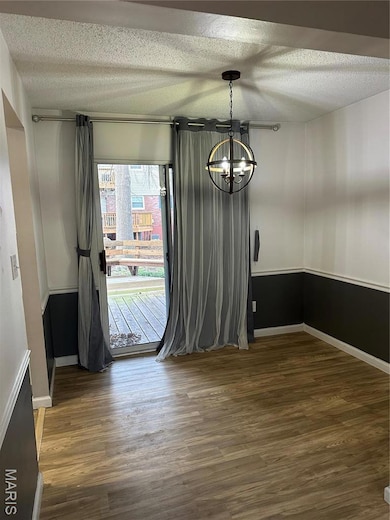 Unfurnished dining area with baseboards, a notable chandelier, wood finished floors, and a textured ceiling