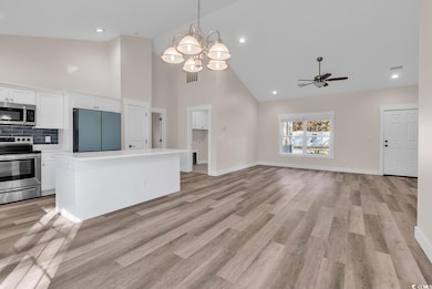 Kitchen featuring appliances with stainless steel finishes, white cabinets, high vaulted ceiling, decorative light fixtures, and light countertops