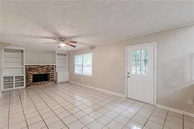 Unfurnished living room featuring light tile patterned flooring, a ceiling fan, a textured ceiling, a brick fireplace, and built in features