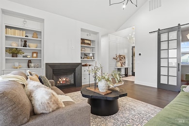 Living room with a barn door, dark wood finished floors, a glass covered fireplace, built in features, and high vaulted ceiling
