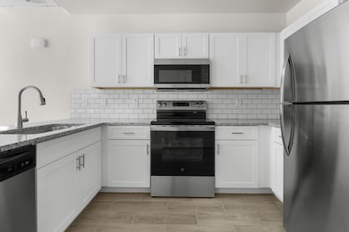 Kitchen with appliances with stainless steel finishes, white cabinetry, light stone countertops, and tasteful backsplash