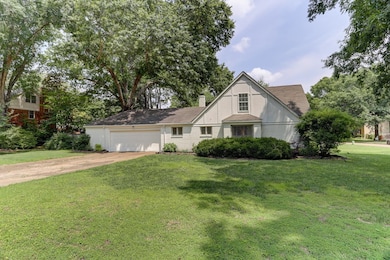 Tudor-style house featuring driveway, an attached garage, a front yard, brick siding, and a chimney