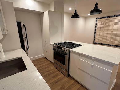 Kitchen with white cabinetry, appliances with stainless steel finishes, light stone counters, decorative light fixtures, and dark wood-type flooring